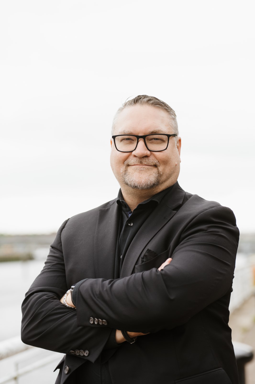 Dr. Jason R. Frank standing outdoors with arms crossed near a waterfront.