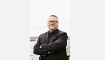 Dr. Jason R. Frank standing outdoors with arms crossed near a waterfront.