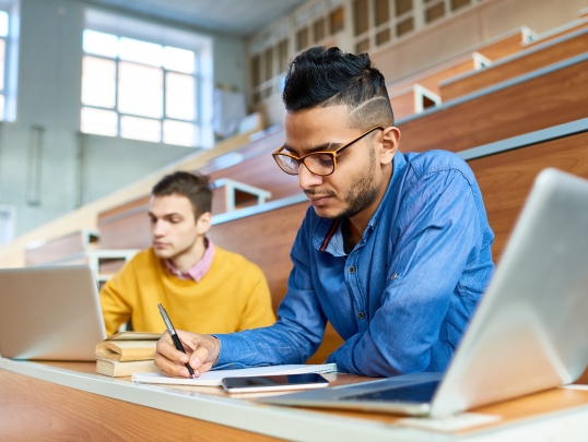A photograph of two students in a lecture hall studying