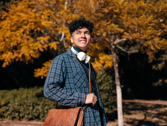 student carrying a bag and posing in front of trees