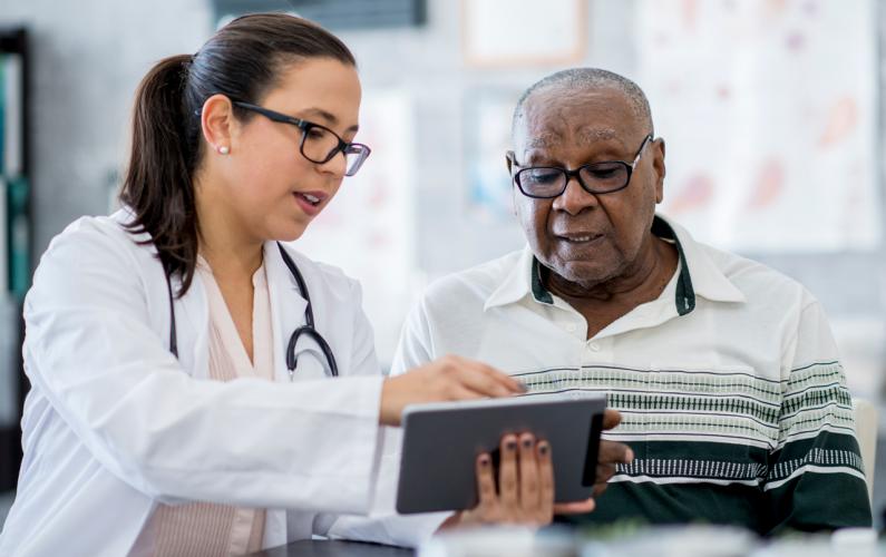 Female doctor showing older male patient something on iPad