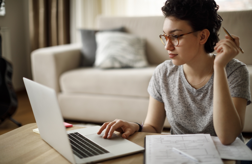 student sitting at desk while taking notes and looking at laptop
